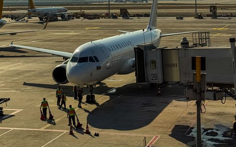 Ein Verkehrsflugzeug mit dem Schriftzug „Azerbaijan“ an einer Fluggastbrücke auf dem Vorfeld des Flughafens Baku, daneben das Bodenpersonal