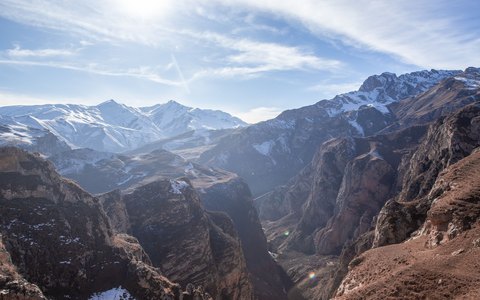 Schneebedeckte Bergkämme über einem tiefen Tal bei Quba unter blauem Himmel mit weißen Wolken