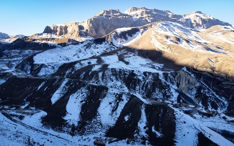 Schneebedeckte Bergkämme bei Laza im Bezirk Qusar, von der tief stehenden Sonne beleuchtet, unter blauem Himmel