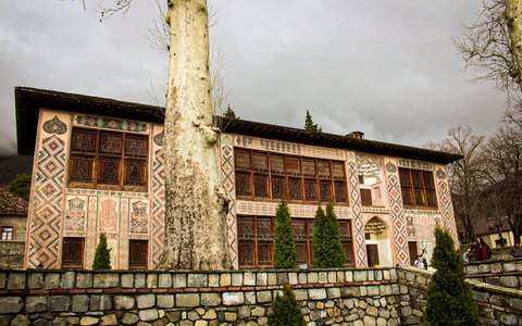 Reich bemalte Fassade des Khanpalasts von Şəki hinter einer hohen Platane und Steinmauer