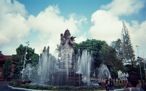 Die Catur-Muka-Statue und Brunnen im Zentrum von Denpasar, mit Bäumen und weißen Wolken