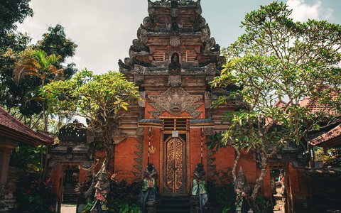 Mit Reliefs verziertes Tor aus rotem Backstein am Palast von Ubud, eingerahmt von Bäumen