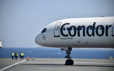 Bug eines weißen Condor-Verkehrsflugzeugs auf dem Vorfeld des Flughafens Heraklion, dahinter Bodenpersonal und Meer