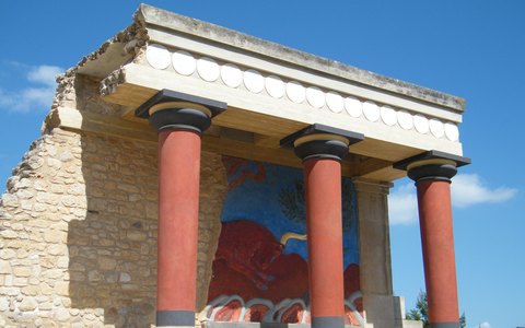 Rote minoische Säulen und ein Stierfresko an einem restaurierten Teil des Palasts von Knossos