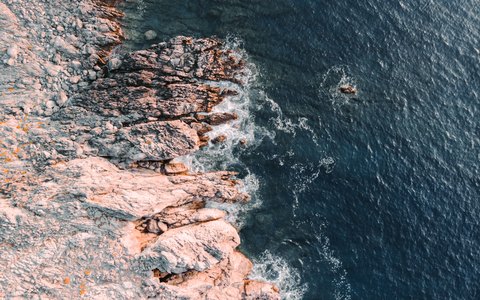 Luftaufnahme rosafarbener Felsen am tiefblauen Meer an der Küste bei Plakias