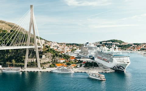 Kreuzfahrtschiffe und kleine Passagierboote im Hafen Gruž in Dubrovnik unter einer weißen Schrägseilbrücke und Häusern am Hang