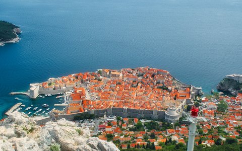 Luftaufnahme der ummauerten Altstadt von Dubrovnik mit roten Dächern auf einer felsigen Landzunge über dem tiefblauen Meer