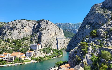 Der Fluss Cetina, der aus einer steilen grauen Schlucht an den Häusern von Omiš vorbeifließt, unter einem klaren blauen Himmel