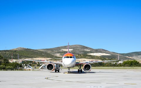Orange-weißes Verkehrsflugzeug auf dem Vorfeld des Flughafens Split, dahinter grüne Hügel unter blauem Himmel