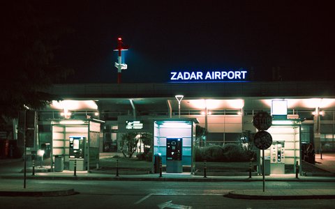 Terminaleingang des Flughafens Zadar bei Nacht mit beleuchtetem Schriftzug „Zadar Airport“