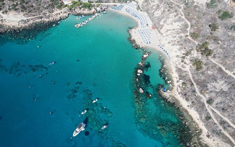 Luftaufnahme einer geschwungenen Sandbucht mit türkisfarbenem Wasser und Booten