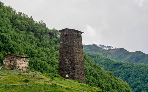 Hoher mittelalterlicher Steinturm am grünen Hang über Mestia vor bewaldeten Bergen