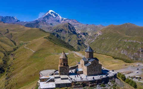 Steinerne Gergetier Dreifaltigkeitskirche auf grünem Bergrücken vor dem schneebedeckten Kasbek unter tiefblauem Himmel