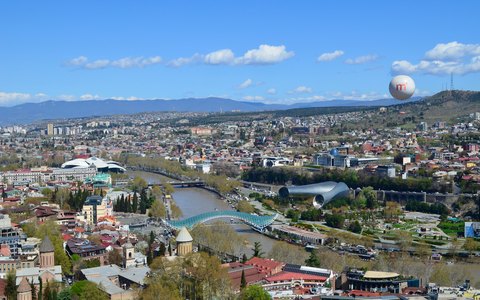 Luftbild von Tiflis am Fluss Kura mit Friedensbrücke unter klarem blauem Himmel