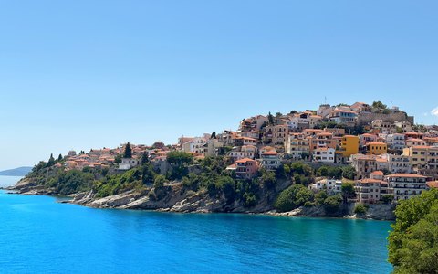 Die Altstadt von Kavala auf einer grünen Landzunge über leuchtend blauem Wasser unter klarem Himmel