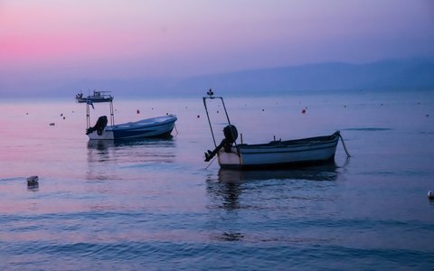 Kleine Boote auf ruhigem Wasser vor dem Strand von Kavos unter rosa Abendhimmel