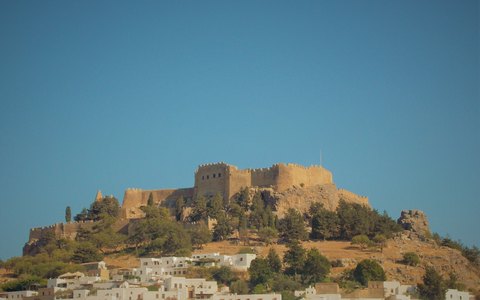 Die Mauern der Akropolis von Lindos auf einer felsigen Anhöhe über weißen Häusern unter blauem Himmel