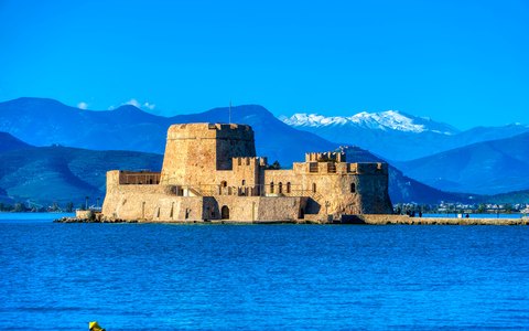 Die kleine steinerne Bourtzi-Festung auf ihrer Insel in tiefblauem Wasser unter blauem Himmel, dahinter Berge