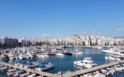 Bootsreihen in der Marina Zeas unter klarem blauem Himmel, dahinter die weißen Gebäude von Piräus