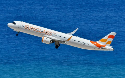 Weißes Verkehrsflugzeug mit orangefarbenen Markierungen am Leitwerk im Steigflug über tiefblauem Meer nach dem Start auf Rhodos