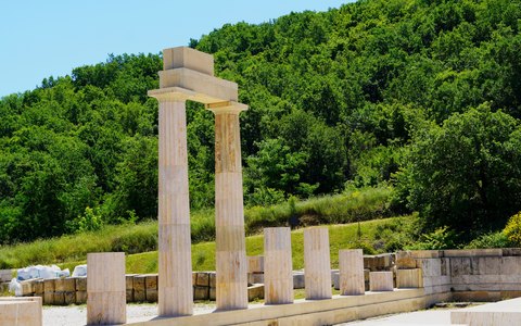 Restaurierte Steinsäulen des antiken Palasts von Vergina vor grünen bewaldeten Hügeln unter blauem Himmel