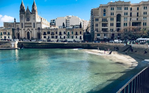 Blick auf die Bucht von St. Julian's mit Booten auf blauem Wasser und historischen Gebäuden am Ufer unter klarem blauem Himmel