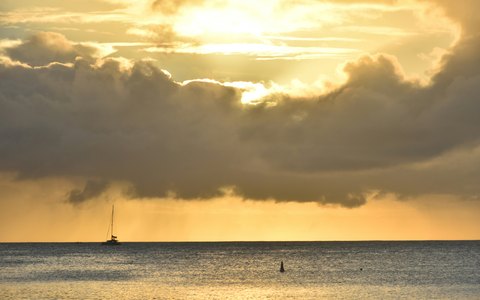 Goldenes Abendlicht, das durch schwere Wolken über einem ruhigen Meer bei Pereybère bricht