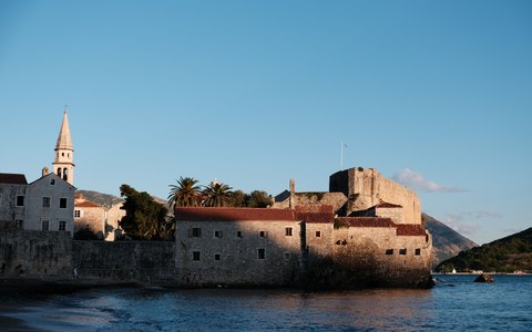 Steinmauern, Glockenturm und rote Dächer der Altstadt von Budva am Wasser