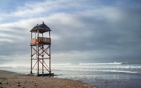 Hölzerner Rettungsschwimmerturm an einem leeren Sandstrand in Agadir mit Wellen und dramatischem Wolkenhimmel