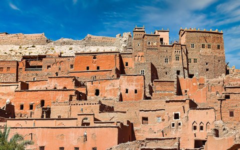 Lehmhäuser und Türme der Kasbah Aït-Ben-Haddou, die sich unter klarem blauem Himmel einen Hügel hinaufziehen