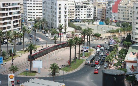 Straßenbahn und Verkehr neben Palmen auf einem von weißen Wohnblöcken gesäumten Platz in Casablanca