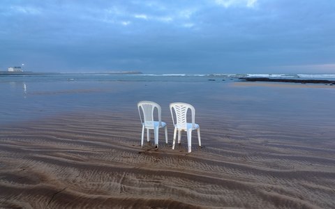 Zwei weiße Plastikstühle im flachen Wasser an einem breiten, flachen Strand bei El Jadida