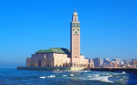 Hassan-II.-Moschee mit hohem Minarett am Ufer von Casablanca, Meereswellen und leuchtend blauem Himmel