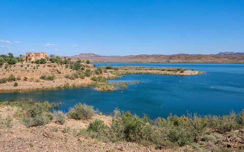 Blaues Seewasser bei Ouarzazate zwischen trockenen Wüstenhügeln unter blauem Himmel