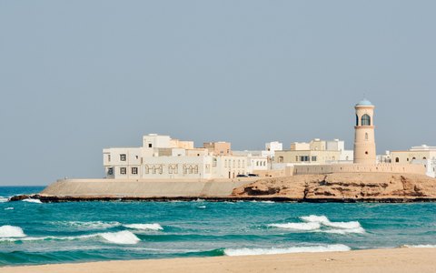 Leuchtturm und traditionelle Gebäude an der Küste von Sur neben blauem Wasser