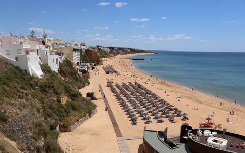 Strand von Albufeira unterhalb von Sandsteinklippen und weißen Gebäuden, mit blauem Meer und klarem Himmel