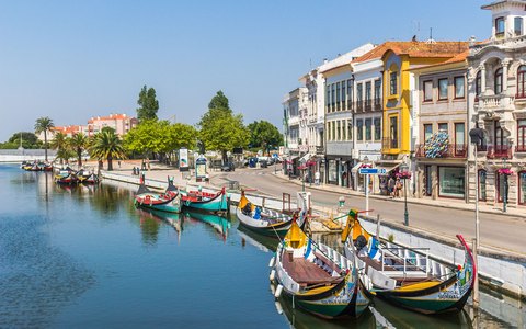Bemalte Moliceiro-Boote, die entlang eines Kanals in Aveiro festgemacht sind, mit Gebäuden der Stadt und hellem Himmel