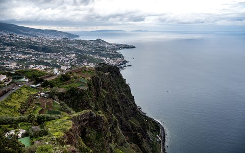 Luftaufnahme der Klippen und der Stadt Câmara de Lobos am Atlantik, dahinter Funchal entlang der Küste