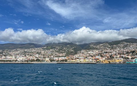 Funchal breitet sich über grüne Hügel oberhalb des blauen Ozeans aus, mit weißen Wolken über den Bergen