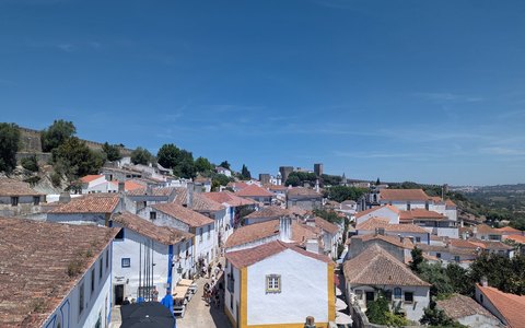 Weiße Häuser mit roten Ziegeldächern im alten ummauerten Dorf Óbidos unter blauem Himmel