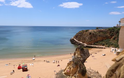 Der breite Sandstrand Praia da Rocha unterhalb goldener Klippen, mit blauem Meer und einigen Wolken