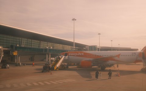 Orange-weißes Verkehrsflugzeug mit Gangway neben dem Terminal des Flughafens Porto im warmen Licht