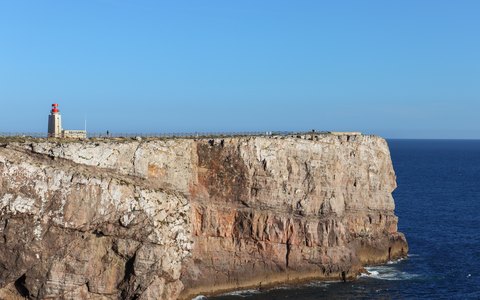 Ein Leuchtturm am Rand einer steilen Klippe an der Landspitze von Sagres über tiefblauem Meer