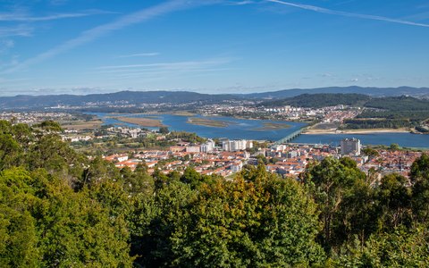 Ein Blick von oben auf Viana do Castelo, den Fluss Lima und grüne Hügel unter blauem Himmel