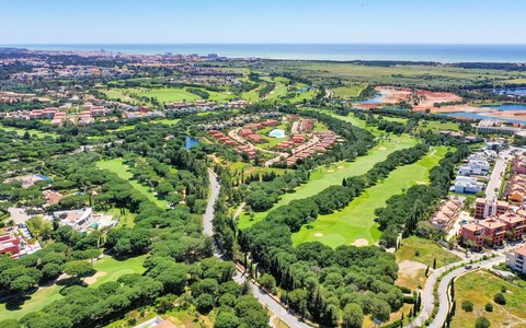 Luftaufnahme grüner Golfbahnen und Pinien zwischen den Villen von Vilamoura, mit dem Meer am Horizont