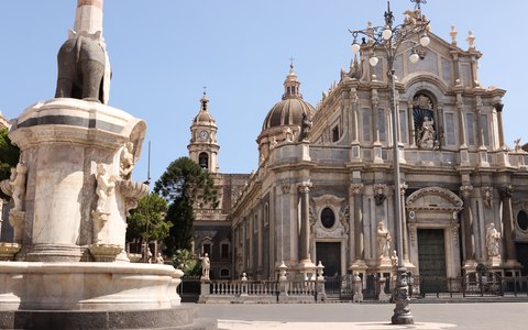 Barockfassade der Kathedrale von Catania neben dem Elefantenbrunnen auf der Piazza Duomo unter leicht bewölktem blauem Himmel