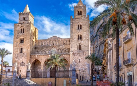 Die normannische Kathedrale von Cefalù mit zwei Türmen und Palmen davor unter strahlend blauem Himmel