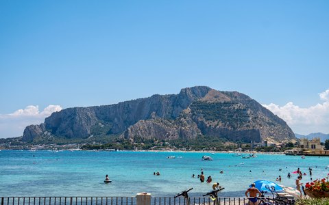 Türkisfarbenes Wasser am Strand von Mondello, dahinter der felsige Monte Pellegrino unter blauem Himmel mit wenigen Wolken