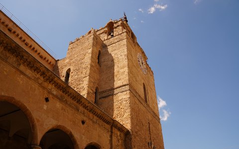 Der goldfarbene steinerne Glockenturm der Kathedrale von Monreale von unten vor leuchtend blauem Himmel