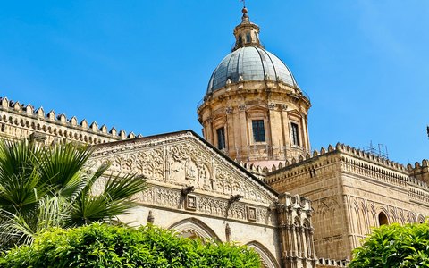 Die verzierte Fassade und Kuppel der Kathedrale von Palermo über Palmen unter klarem blauem Himmel